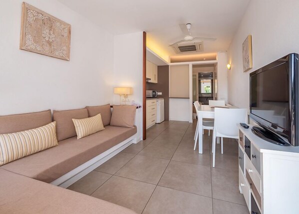 A modern living room with a sofa, TV, and dining area. - Hotel Calina (Cadaqués)