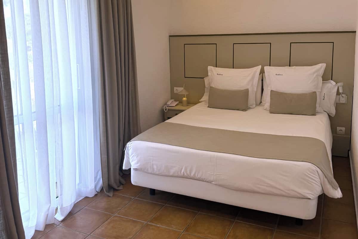 Habitación de hotel con cama, cortinas, mesita de noche y una lámpara en el techo.
