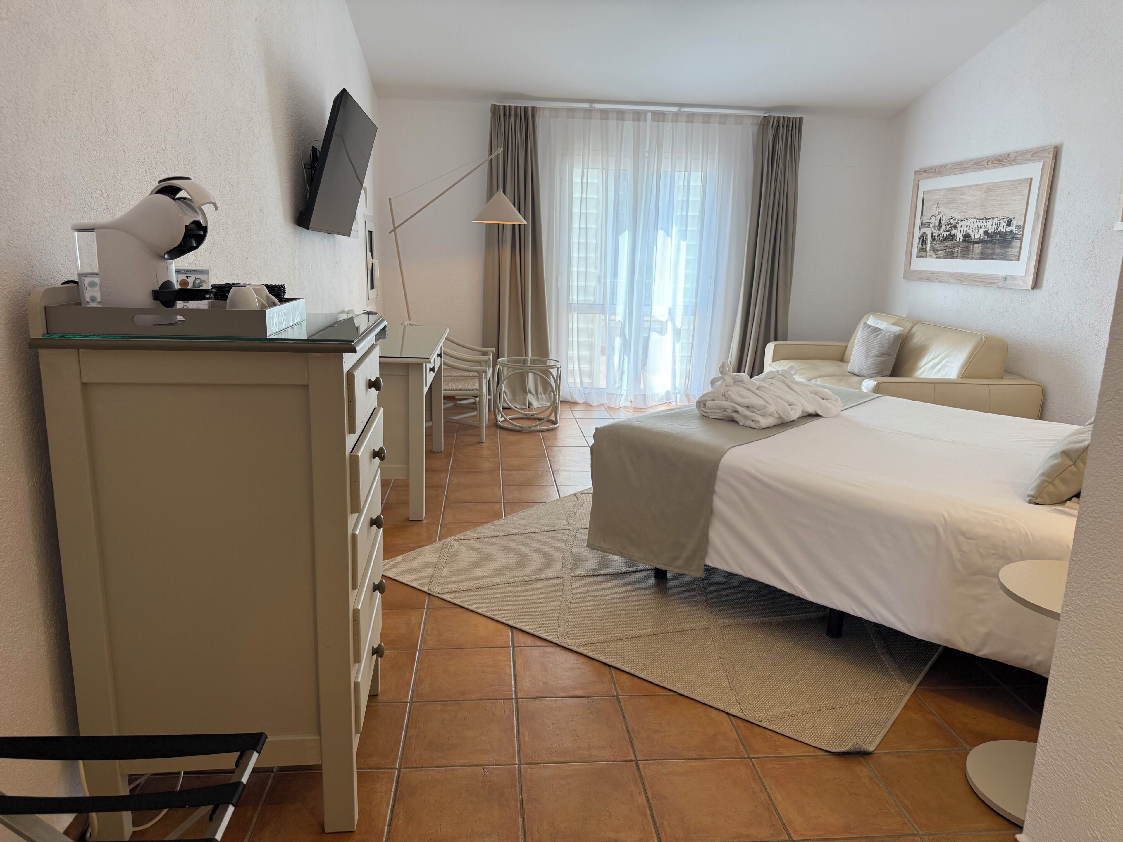 Habitación de hotel con cama, escritorio, silla, televisor y ventana con cortinas.