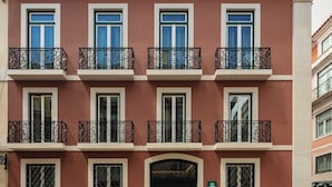 A multi-story building with a red facade, multiple balconies with wrought iron railings, and a green door at the ground level.