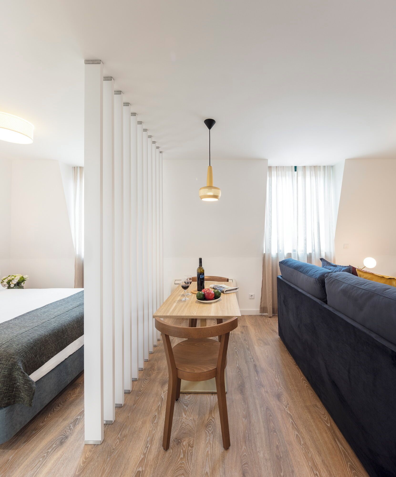 Una habitación moderna y bien iluminada con una mesa de comedor de madera, un sofá y una cama.
