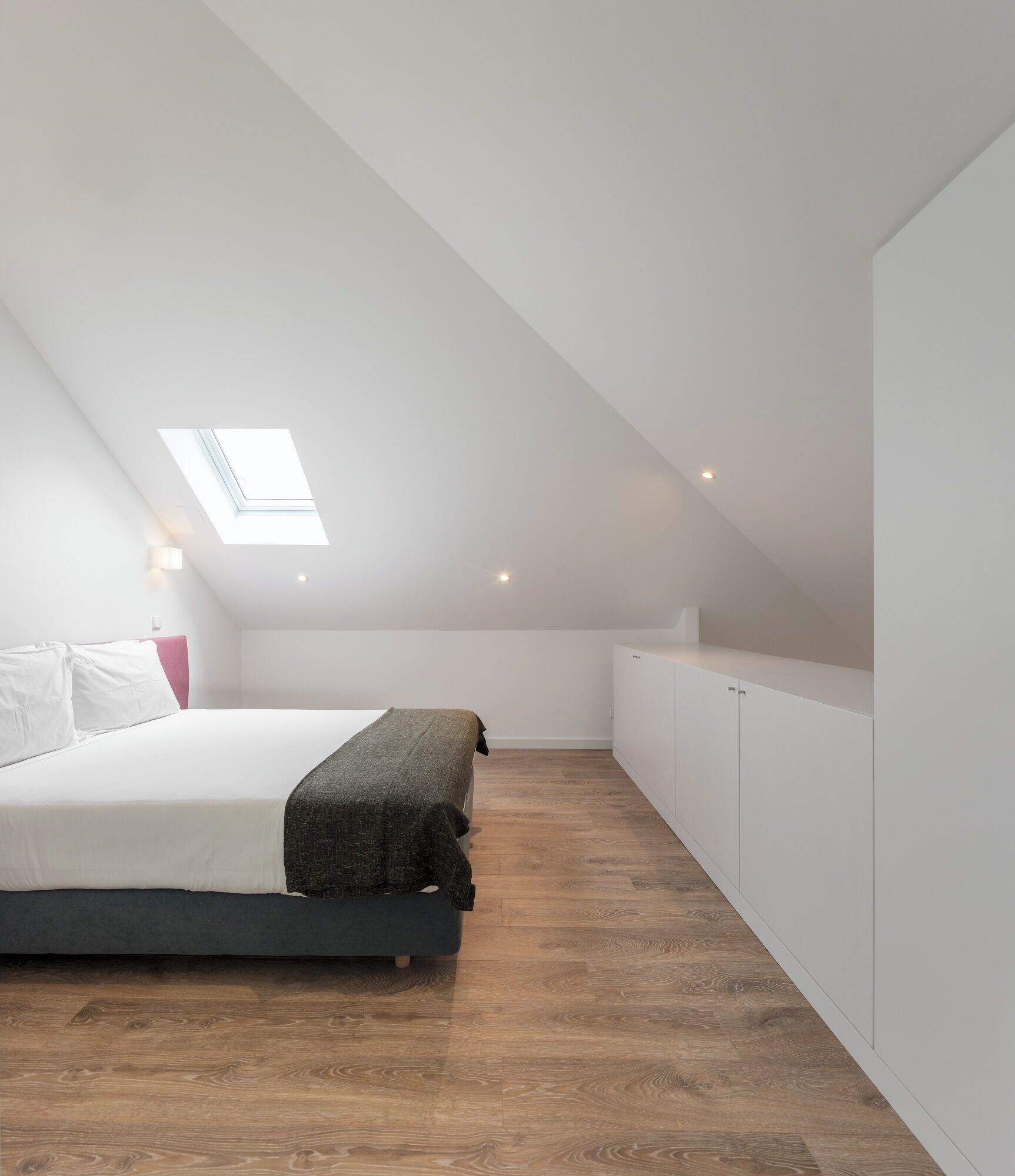 A modern bedroom with a skylight, a bed, and wooden flooring.