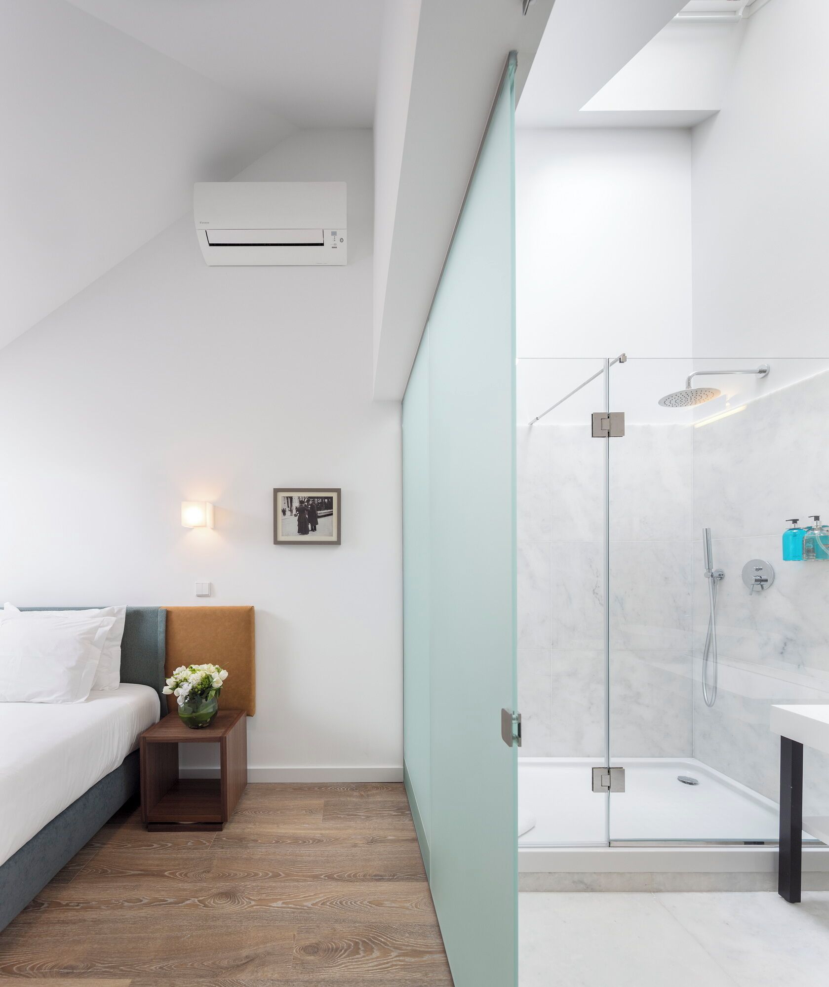 Una habitación de hotel moderna con una cama, una mesita de noche y una zona de ducha con paredes de vidrio.
