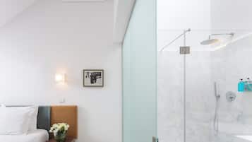 Una habitación de hotel moderna con una cama, una mesita de noche y una zona de ducha con paredes de vidrio.