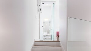 A modern staircase with wooden steps and glass railings, leading to a bathroom with a glass shower enclosure.
