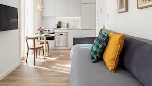 A modern, well-lit apartment with a kitchen, dining area, and a living room with a sofa and cushions.