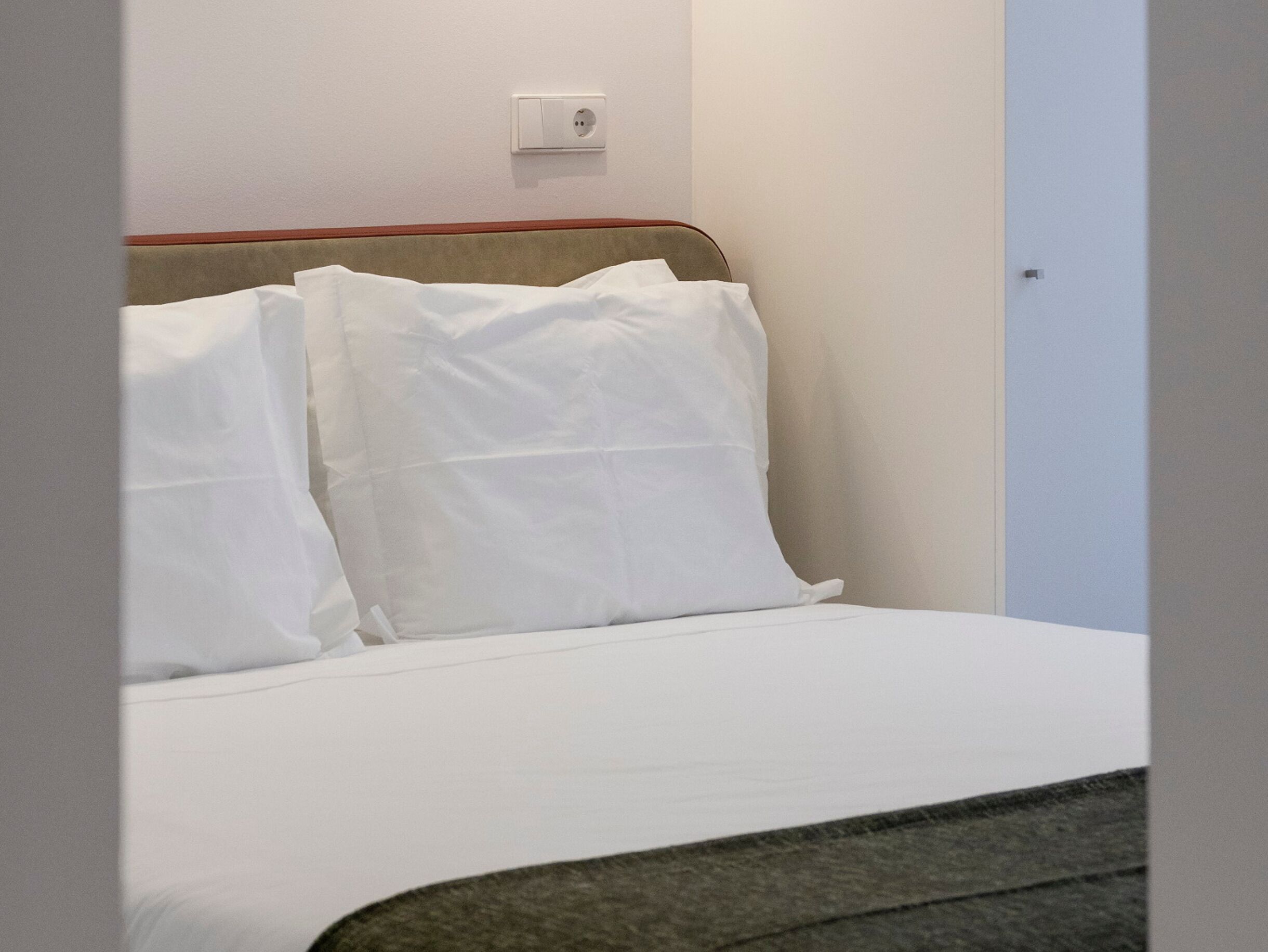 A bed with white linens and a headboard with a wooden panel.