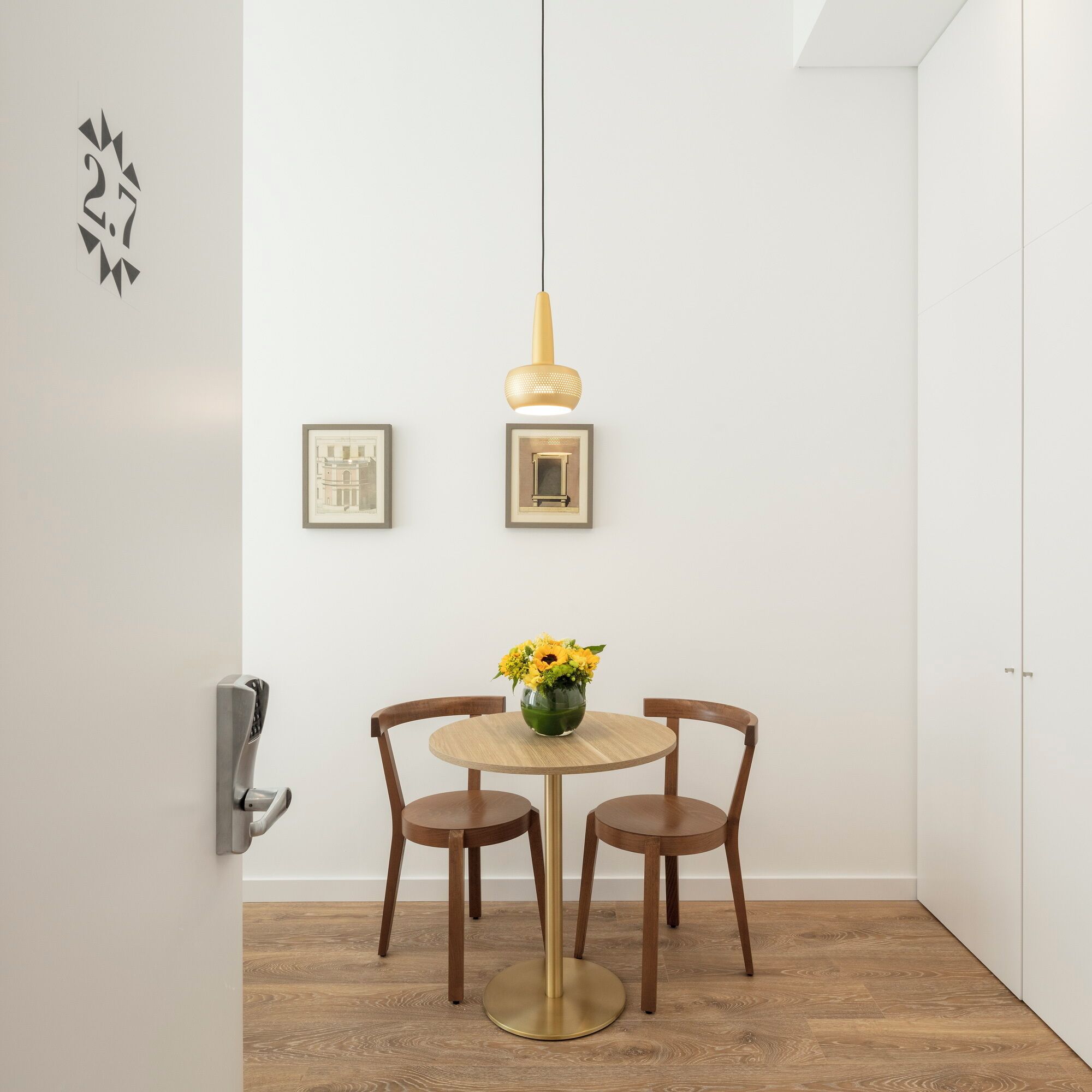 Comedor con una mesa redonda, dos sillas, un jarrón con flores y dos cuadros en la pared.