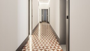 A modern hallway with geometric patterned flooring, white walls, and a ceiling with linear lighting.