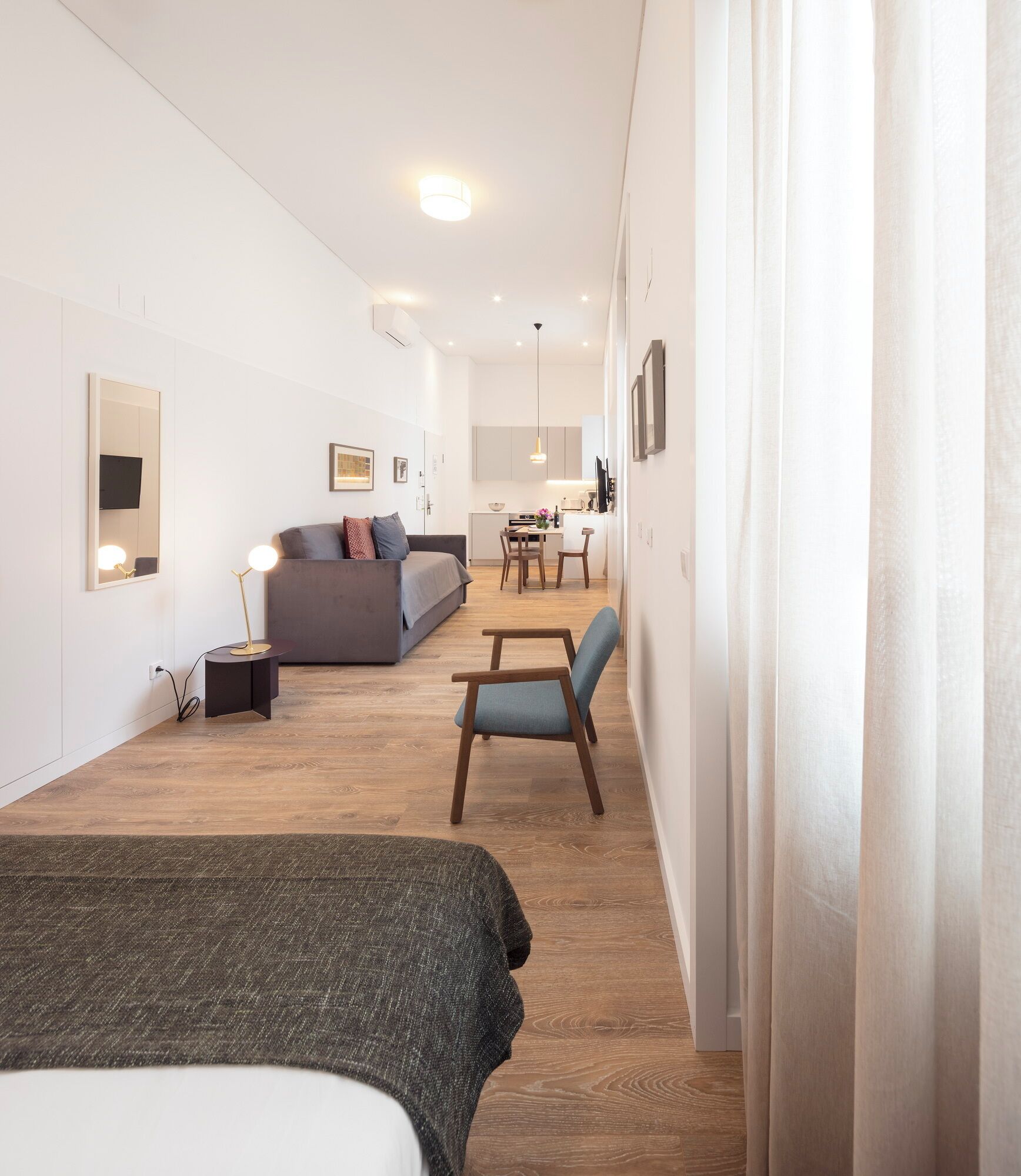 A modern, well-lit room with a bed, a sofa, a dining table, and a chair.