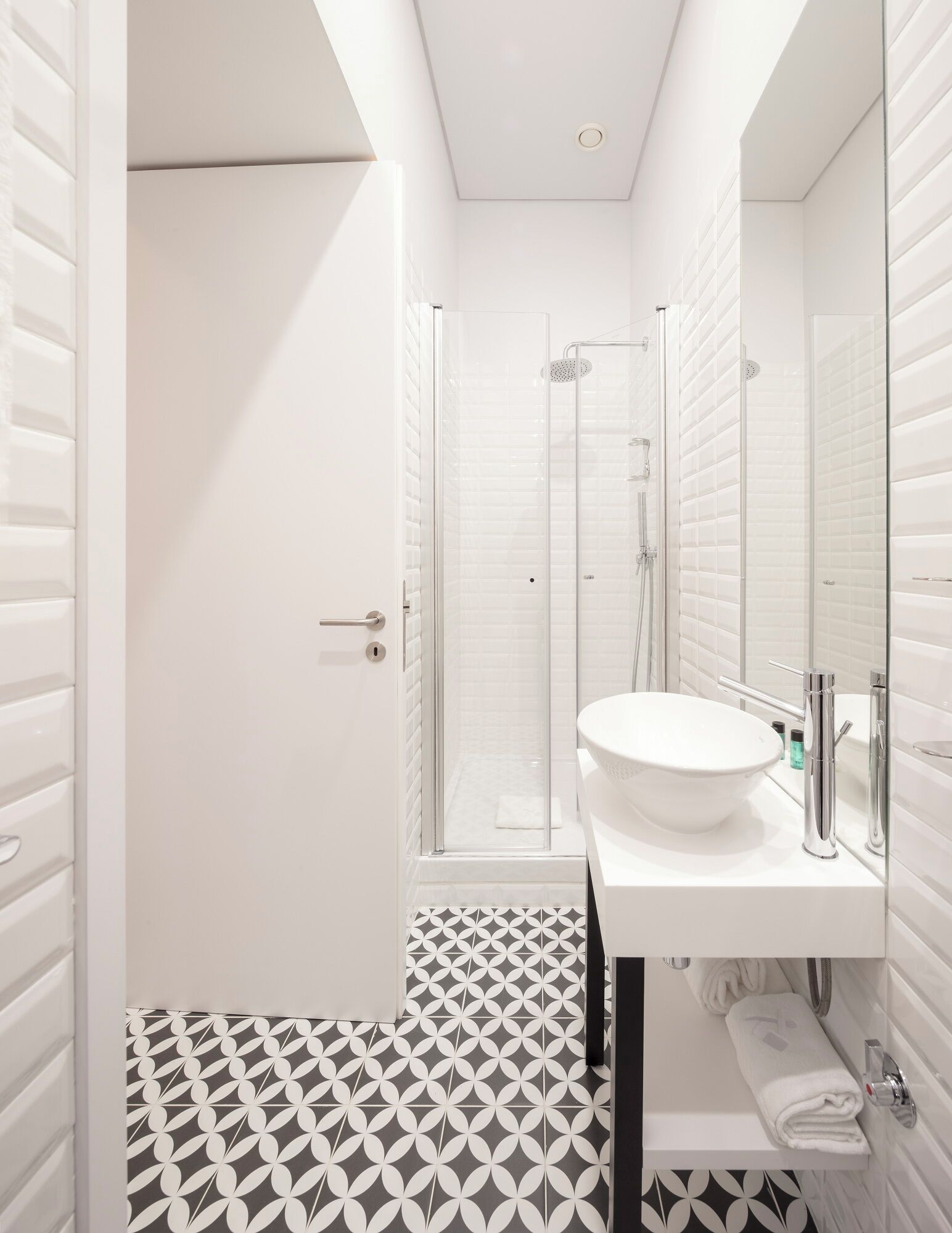 A modern bathroom with a white sink, a glass shower enclosure, and a patterned floor.