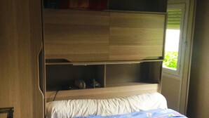 A compact bed with a colorful quilt, a small bedside table, and a shelf above the bed. - Camping les Craoues (Capvern)