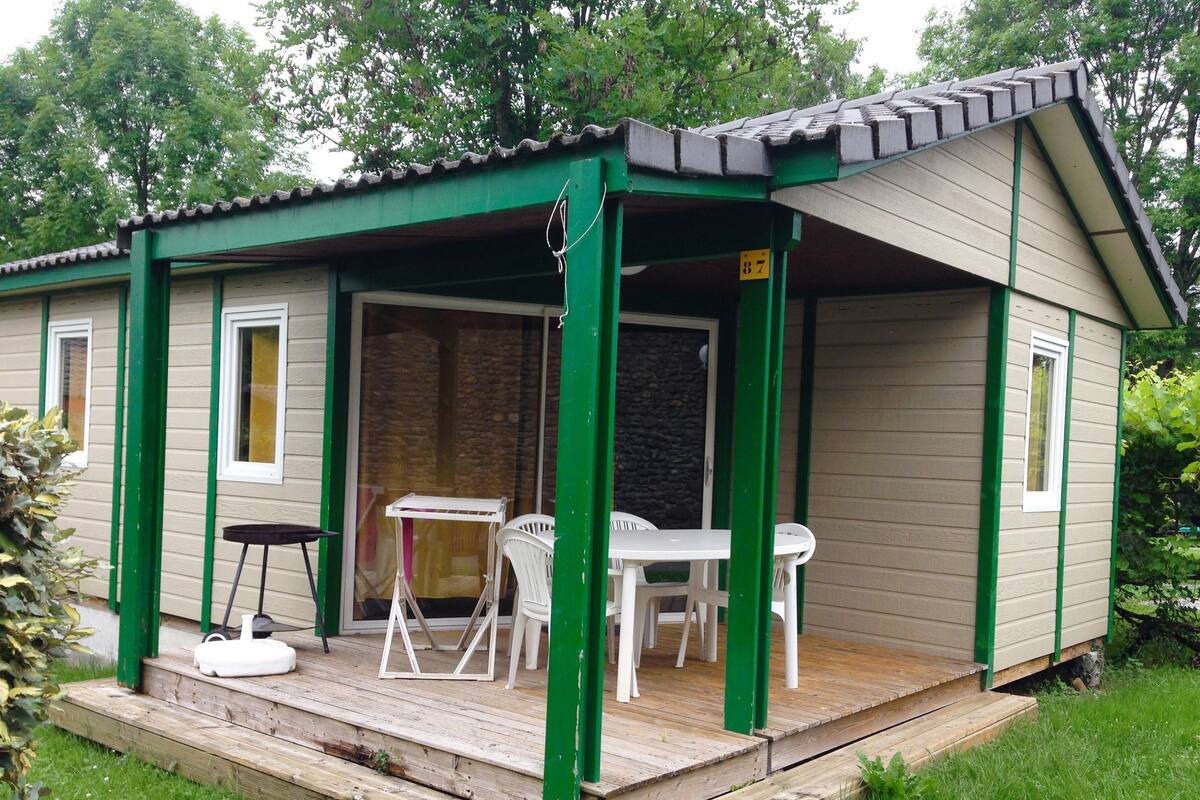 Ein kleines, eingeschossiges Gebäude mit Gründach und einer überdachten Veranda. Auf der Veranda stehen ein Tisch und zwei Stühle, und im Inneren ein kleiner weißer Tisch mit einem Stuhl.