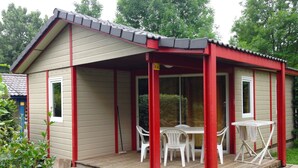 A small, single-story building with a covered porch and a table with chairs. - Camping les Craoues (Capvern)