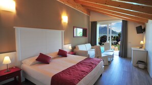 A hotel room with a large bed, a sofa, a small table, and a view of mountains and a lake. - Hotel Resort Le Vele (Domaso)
