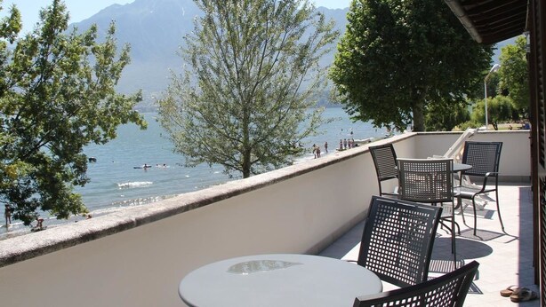 Ein Balkon mit Tisch und Stühlen mit Blick auf einen See, im Hintergrund Berge.