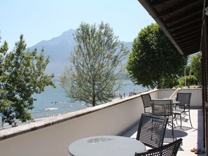 Un balcón con mesa y sillas que da a un lago con montañas al fondo.