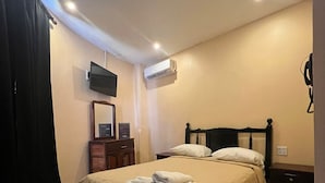 A bedroom with a bed, a TV mounted on the wall, an air conditioning unit, and a bedside table. - La Cubana Hotel & Residencial (Colon)