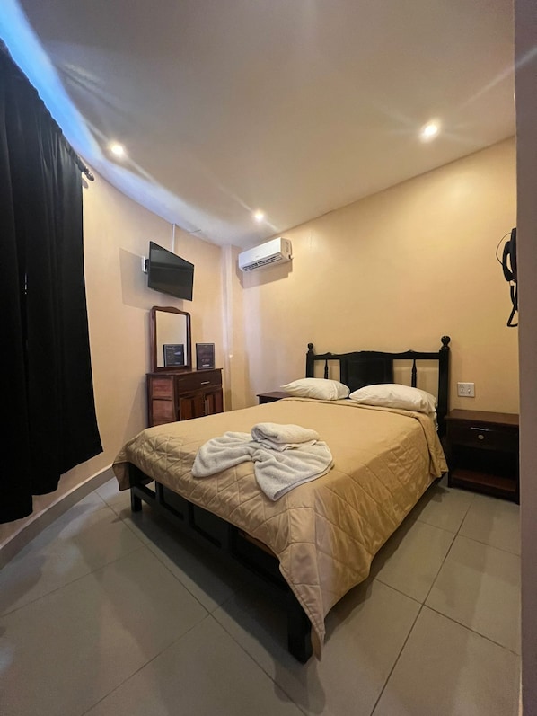 Un dormitorio con cama, televisor montado en la pared, aire acondicionado y mesita de noche.