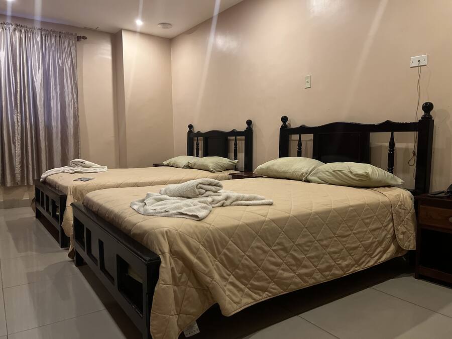 A hotel room with two beds, beige bedding, wooden headboards, a nightstand, and a power outlet on the wall.