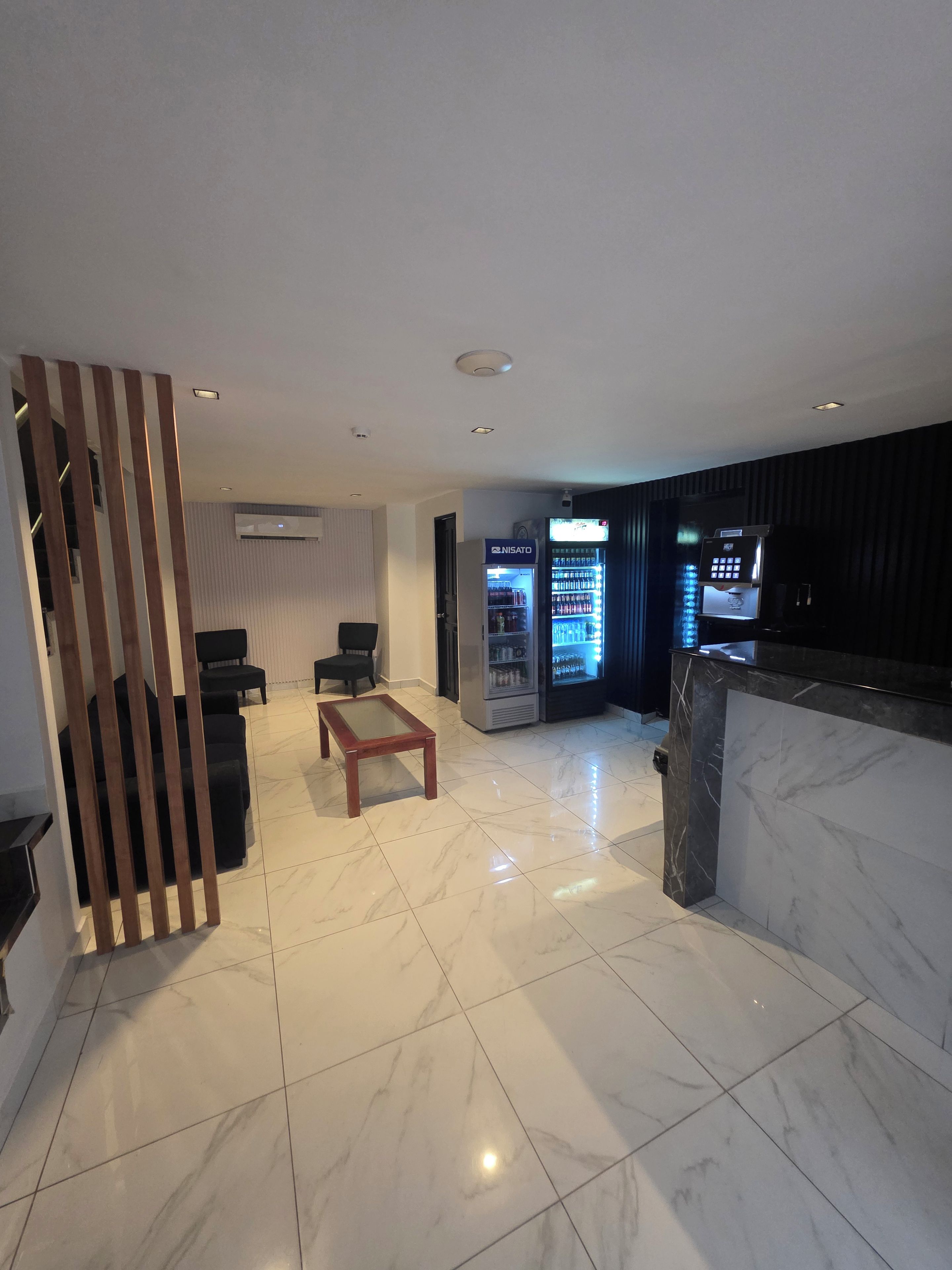 A modern hotel lobby with a marble floor, seating area, vending machines, and a reception desk.