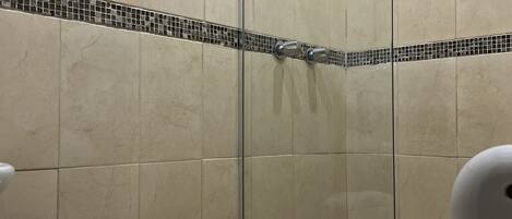 A bathroom with a toilet, a shower with a glass door, and a tiled wall.