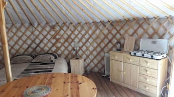 Una yurta acogedora con interior de madera, una cama, una mesita y una kitchenette con estufa.
