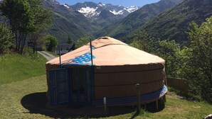 Una yurta tradicional con una entrada de patrón azul, ubicada frente a montañas y un cielo despejado.