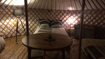 Una yurta acogedora y con poca luz, que incluye una cama, una mesita y una lámpara.