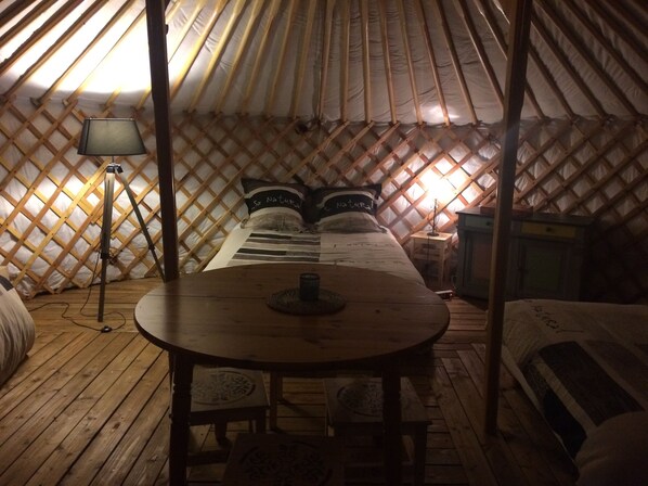 Una yurta acogedora y con poca luz, que incluye una cama, una mesita y una lámpara.