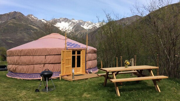 Una yurta con puerta de madera, una mesa de picnic y una parrilla en el exterior.