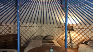 Interior de una yurta tradicional con una cama de madera, una mesa redonda y una lámpara colgante.