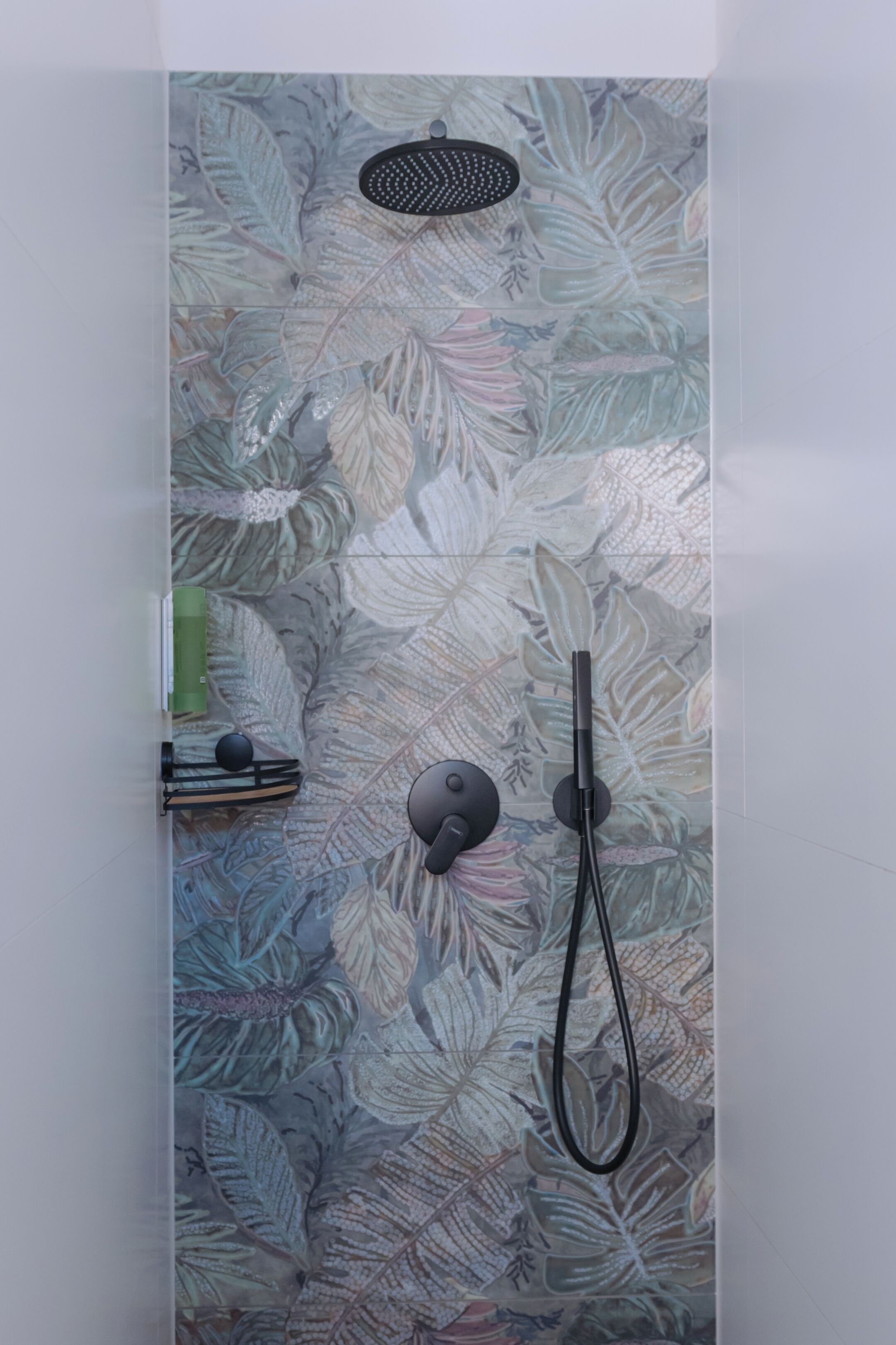 A shower with a leaf-patterned tile wall, a handheld showerhead, and a wall-mounted control.