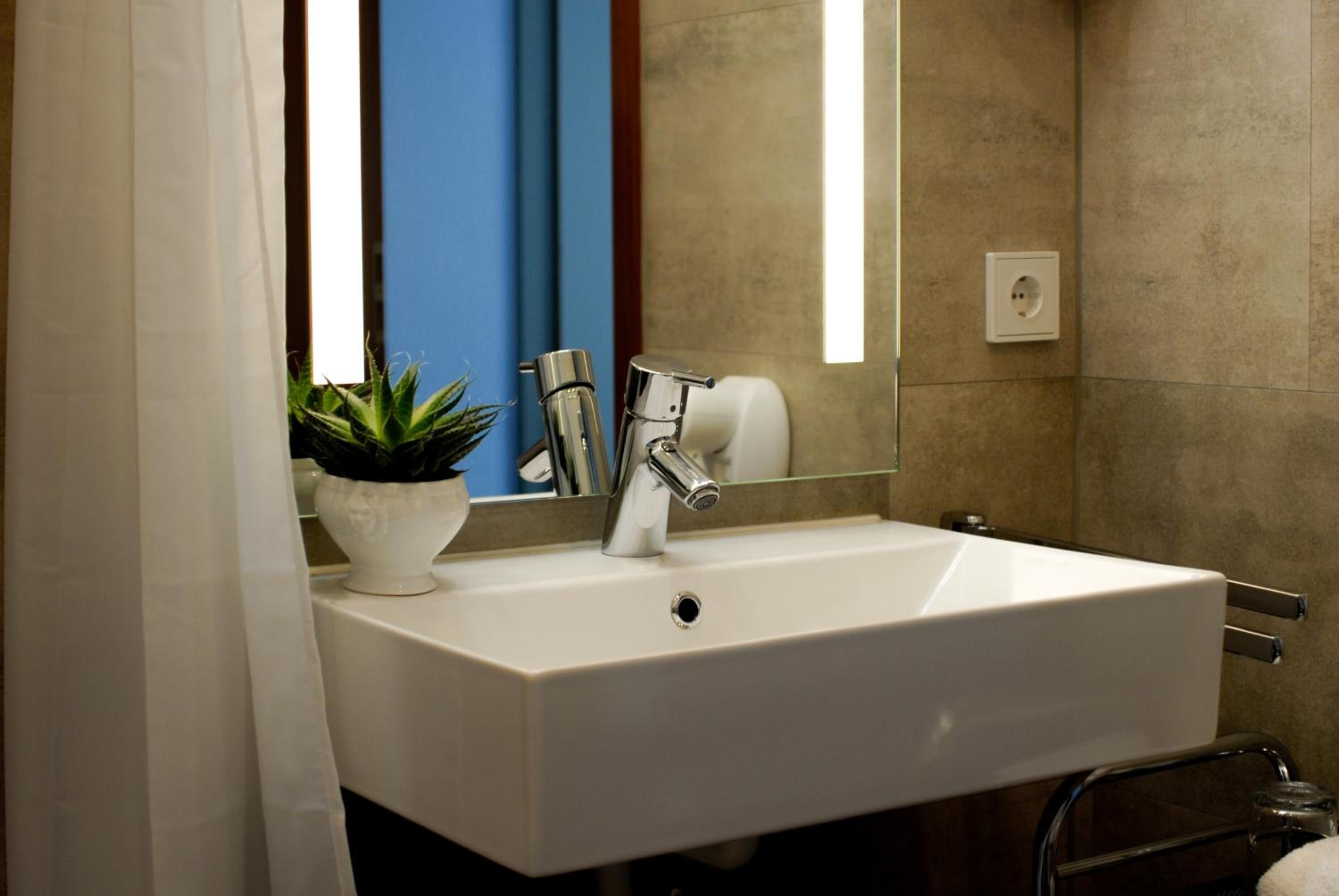 A modern bathroom with a white sink, chrome faucet, and a mirror above it.