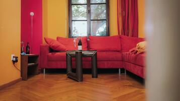 Ein Zimmer mit einer roten Couch, einem kleinen Tisch und einem Fenster mit Vorhängen.