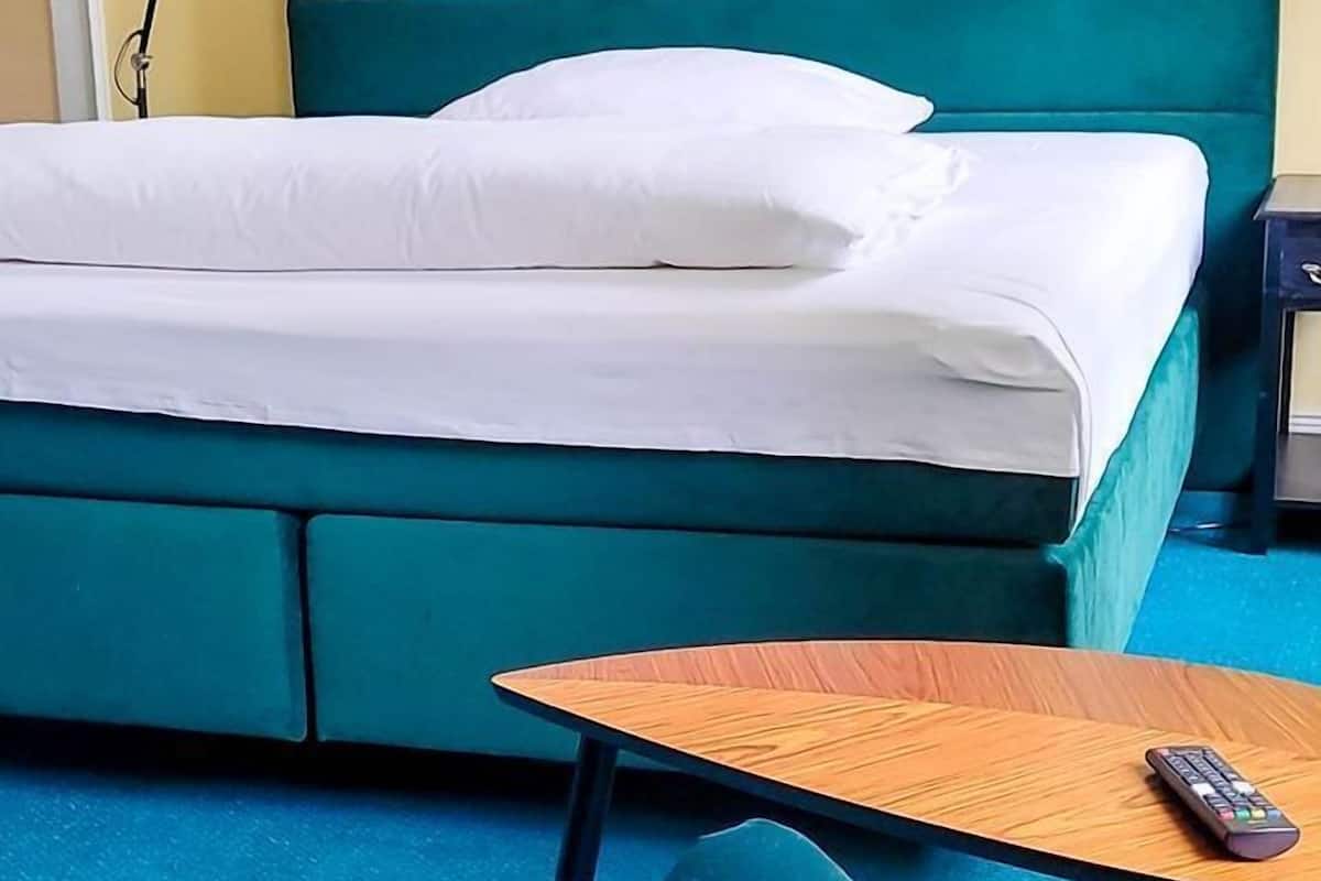 Quarto com cama, escrivaninha e cadeira. Há um quadro na parede e um controle remoto sobre a escrivaninha.