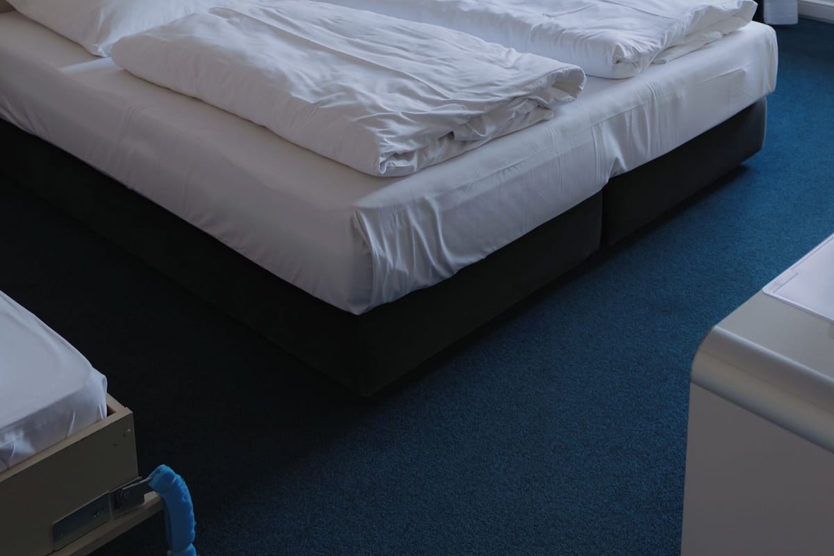 Quarto de hotel com uma cama grande, uma cadeira, uma escrivaninha, um abajur e um quadro na parede.