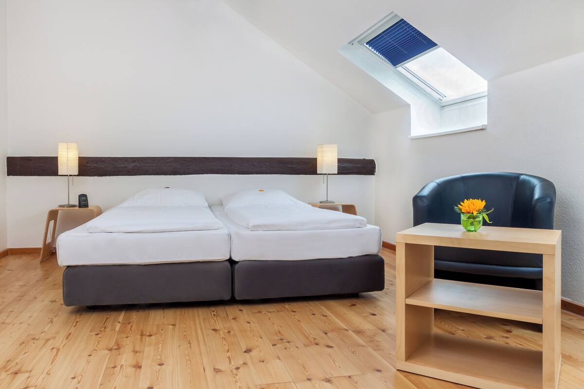 Um quarto com cama, poltrona, mesinha e claraboia.