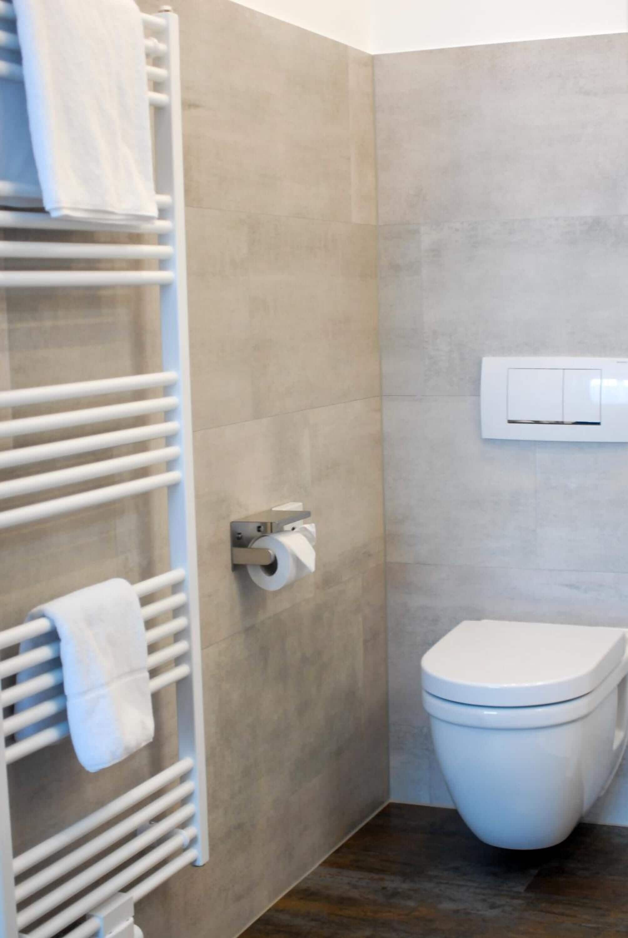 Un baño moderno con un inodoro blanco, un perchero con toallas y un dispensador de papel higiénico.