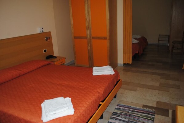 Habitación de hotel con cama de madera, mesita de noche y teléfono. Se ve una puerta que conduce a otra habitación con cama.