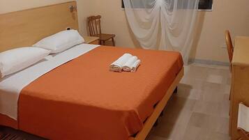 Ein Schlafzimmer mit einem Bett, einem Schreibtisch, einem Stuhl und einem Fenster mit durchsichtigen Vorhängen.