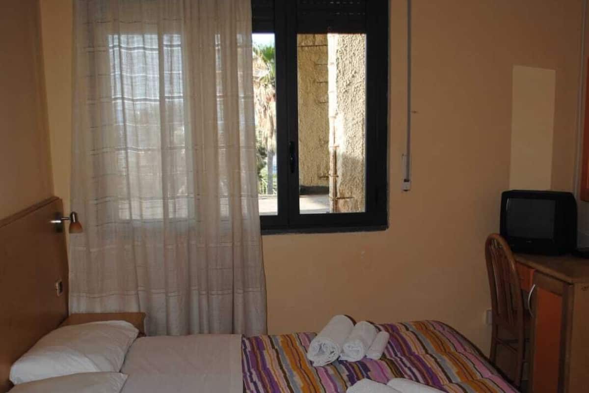 A hotel room with a bed, a desk, a television, and a window with curtains.