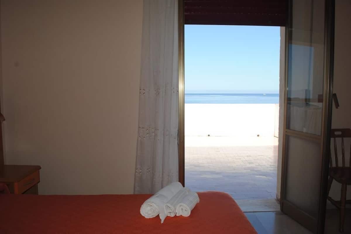 A room with a bed, a window, and a view of the beach.