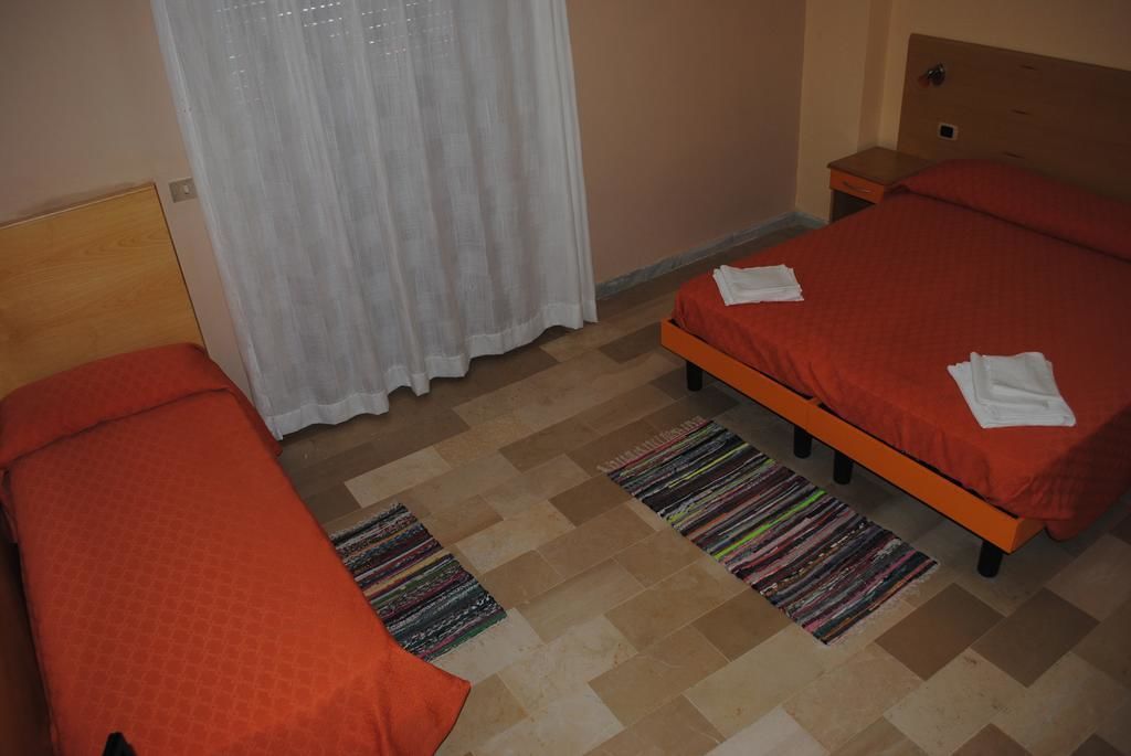 Une chambre avec deux lits, une tête de lit en bois, une table de chevet et une fenêtre avec des rideaux blancs.