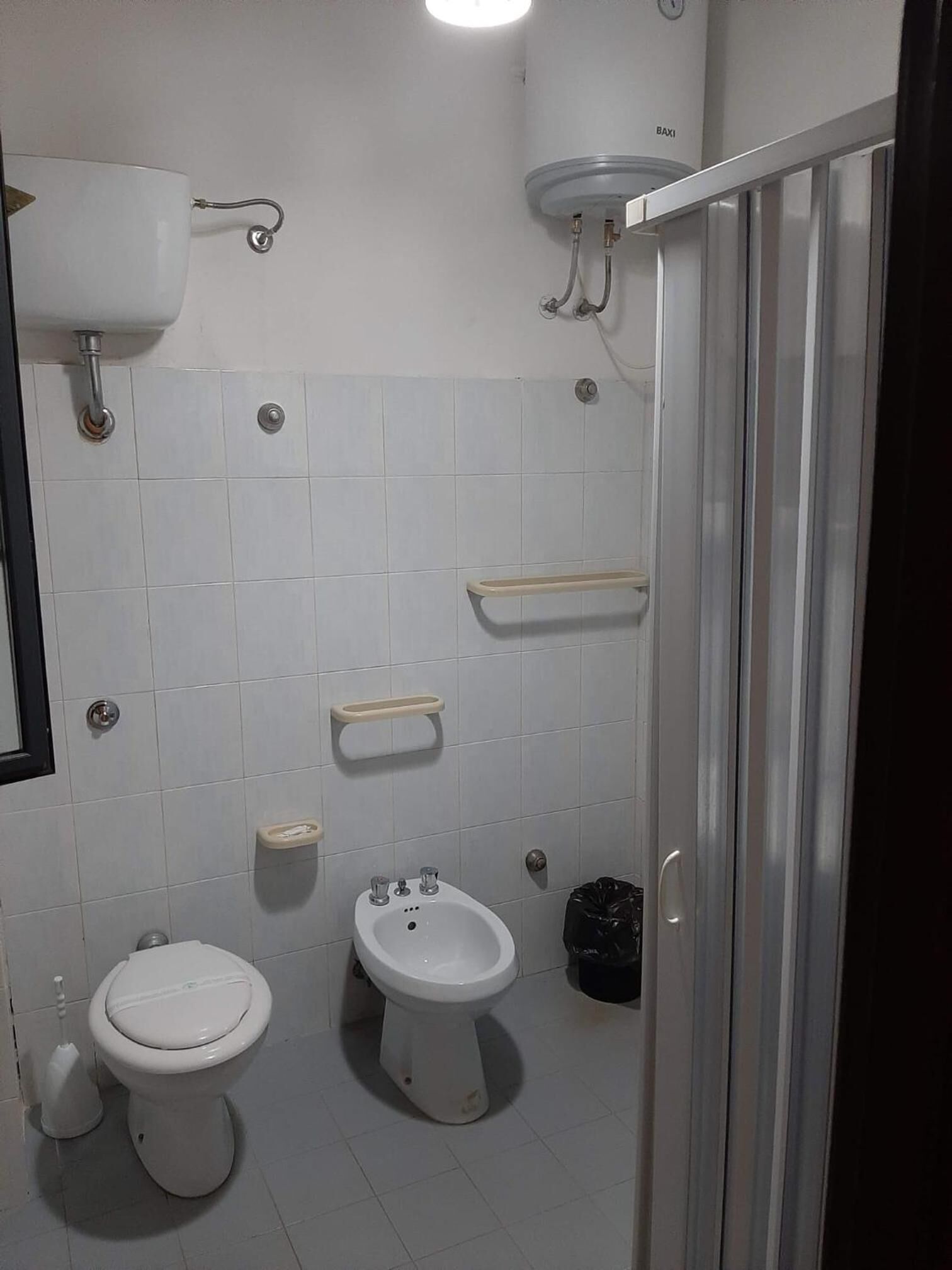 Une petite salle de bain carrelée, équipée de toilettes, d’un bidet et d’un lavabo.