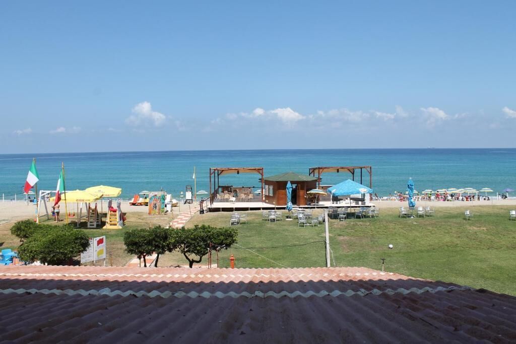 A beachside property with a wooden structure, outdoor seating, and a view of the sea.