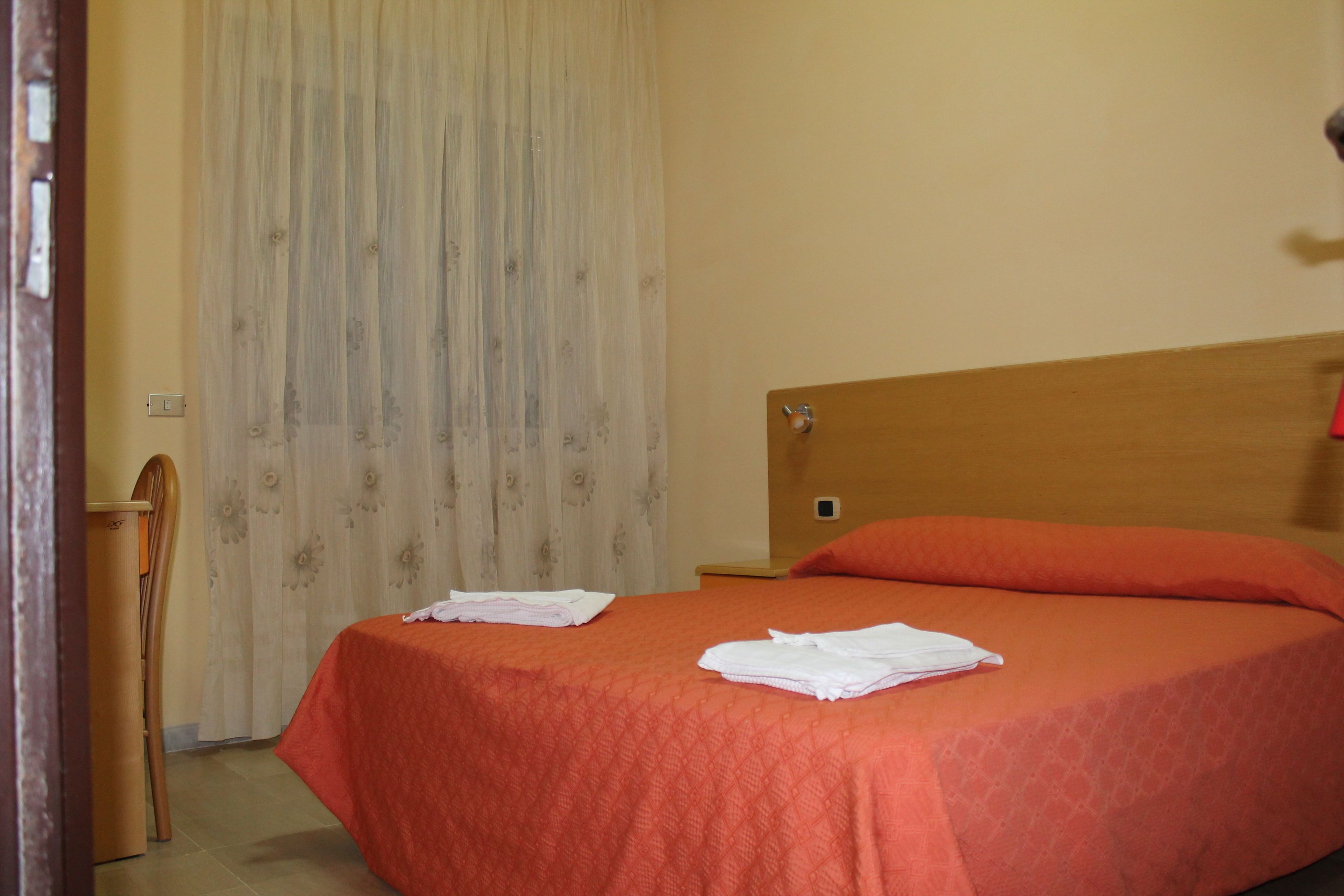 Ein Hotelzimmer mit einem Bett, einem hölzernen Kopfteil, einem Sessel und einem Vorhang.