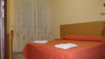 Ein Hotelzimmer mit einem Bett, einem hölzernen Kopfteil, einem Sessel und einem Vorhang.