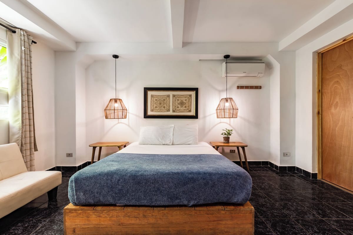 Ein modernes Schlafzimmer mit einem großen Bett, zwei Nachttischen, einer hölzernen Bank, einer Topfpflanze und einer großen Holztür.