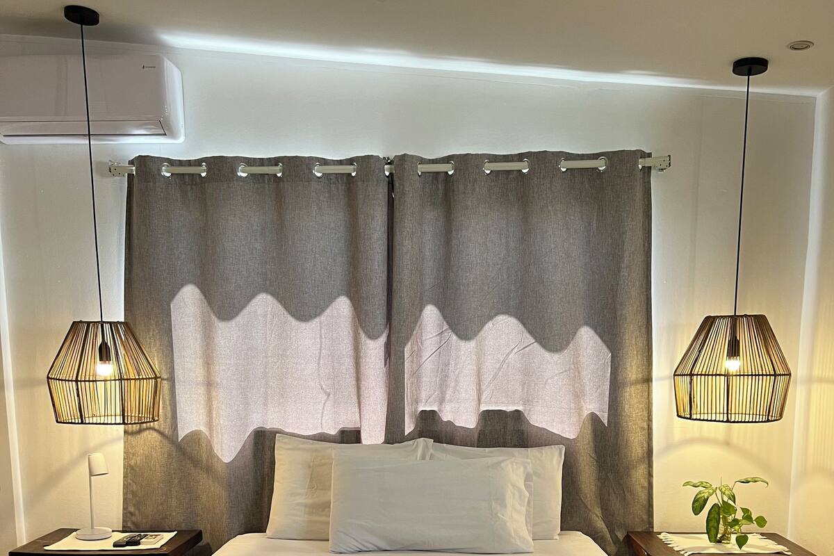 Ein Schlafzimmer mit einem großen Bett, zwei Nachttischen, einem Beistelltisch, einer Zimmerpflanze und einem Deckenventilator.